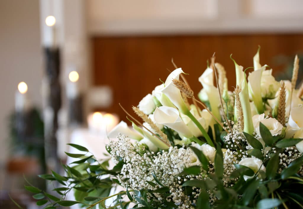 Élégant bouquet de lys calla blancs, gypsophile et épis de blé. Lumières de bougies floues créent une ambiance douce.